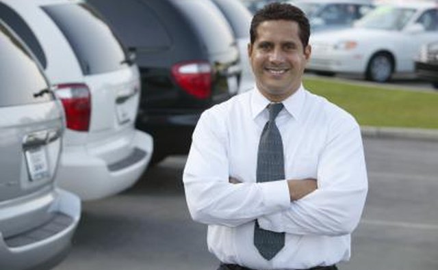 A car salesman stands in his dealership lot
