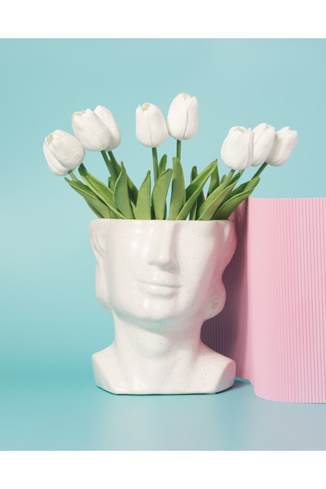 Concrete head sculpture with tulip flowers on a pastel blue background.