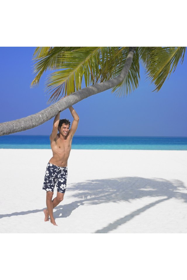 Man hanging on palm tree at beach