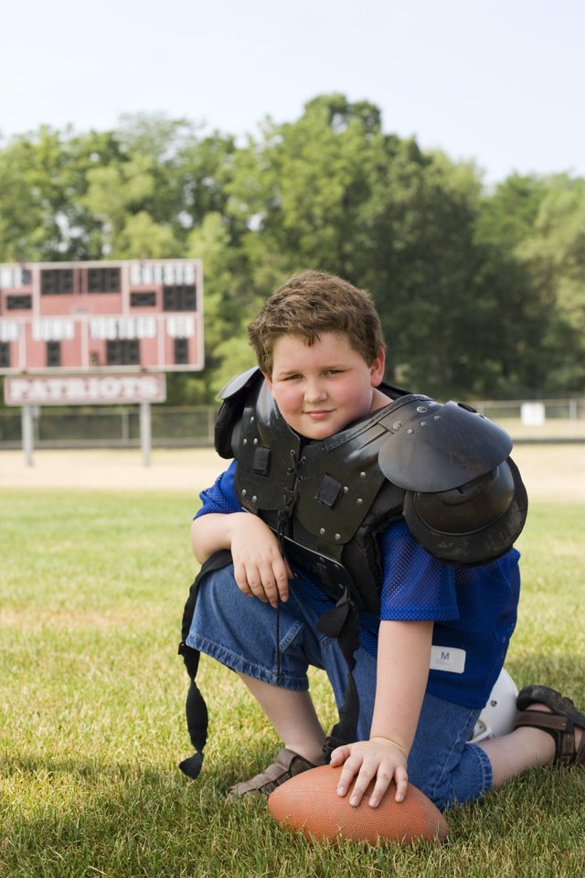 Boy in football pads kneeling on ground with football