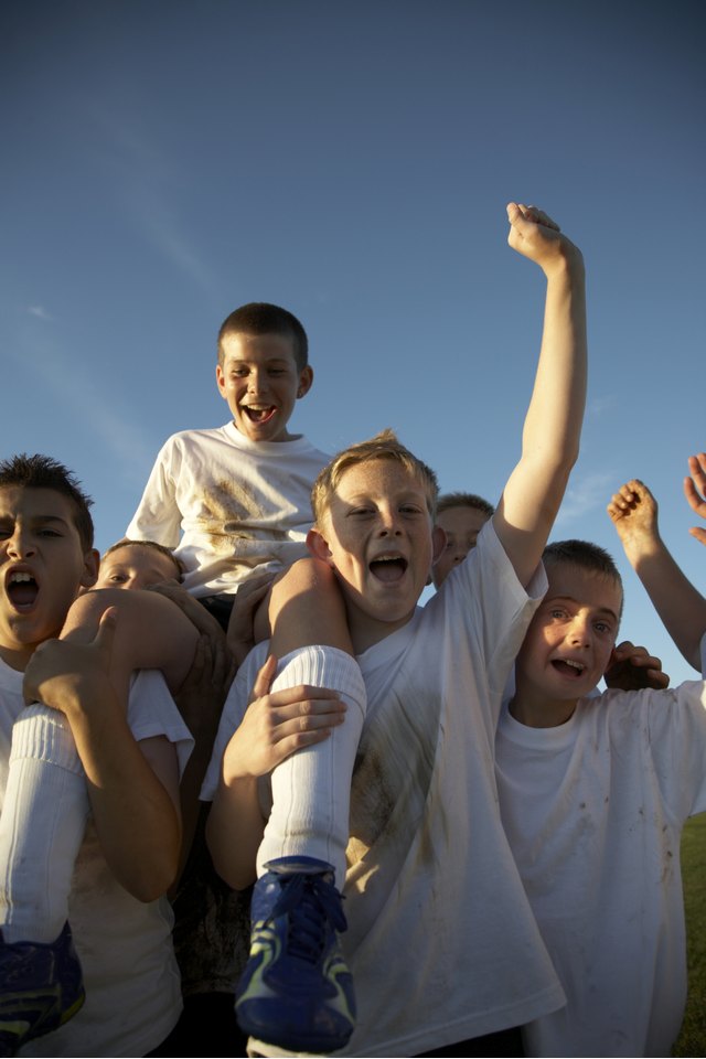 Boys (11-13) in football team carrying team mate on field, cheering