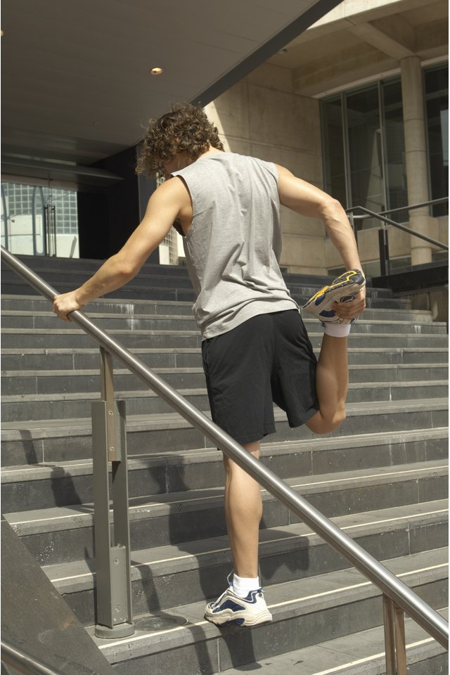 Young man stretching thigh on steps, rear view