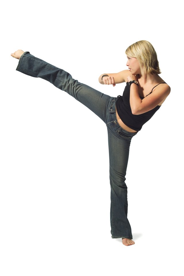 a young caucasian blonde woman in jeans and a black tank top strikes a martial arts pose