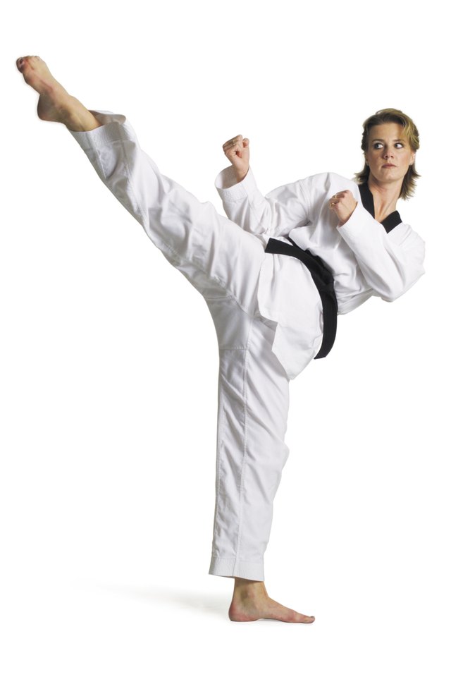 adult caucasian female martial arts expert in white with blackbelt performs roundhouse kick to right