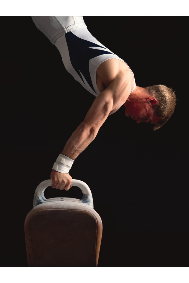 a strong male gymnast does a handstand on the pommel horse