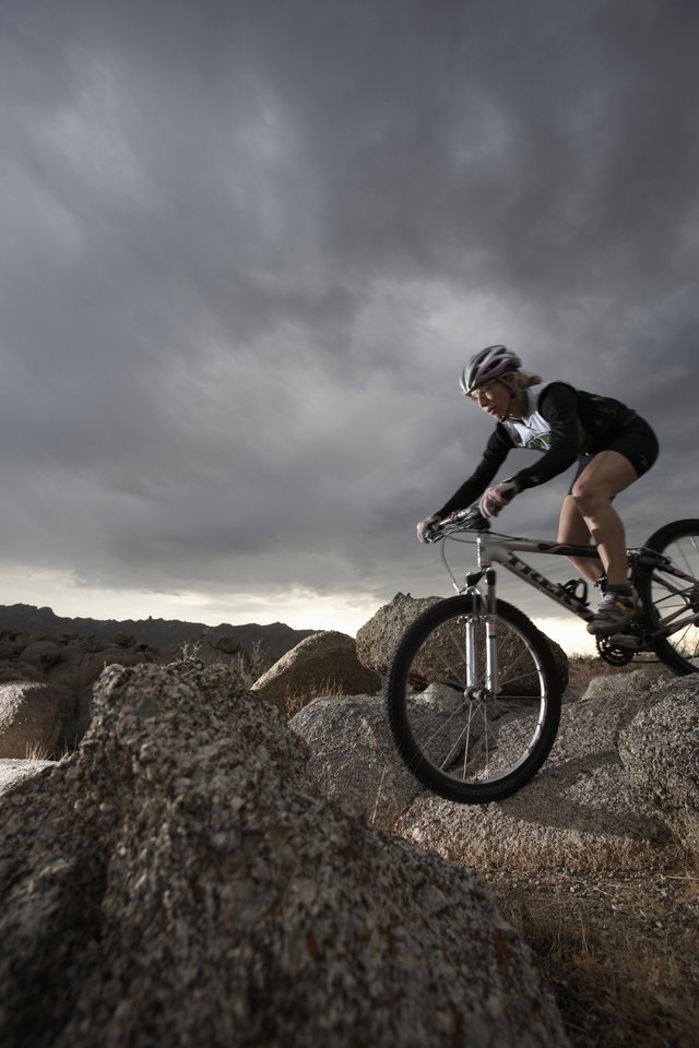 Female rider mountain biking between rocks, side view