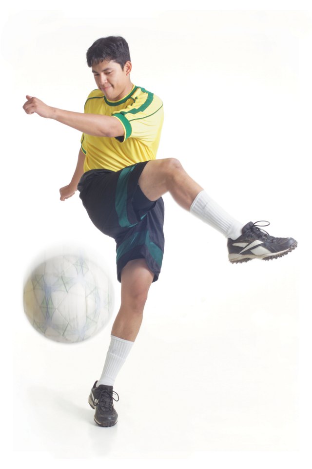a young latin male wears a yellow soccer jersey and powerfully kicks the ball away