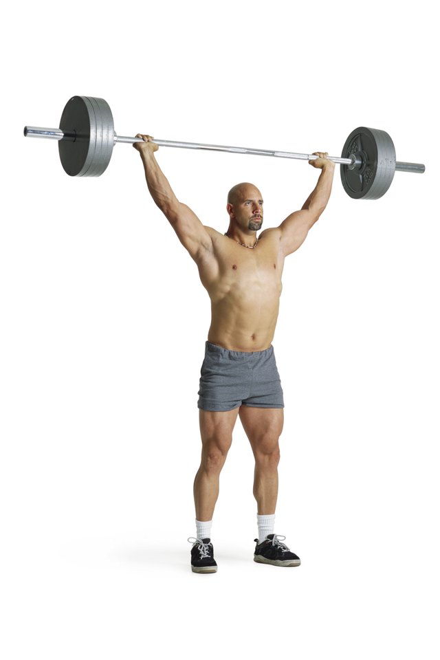 an adult caucasian male weightlifter in gray shorts stands with an extremely heavy weight raised high above his head