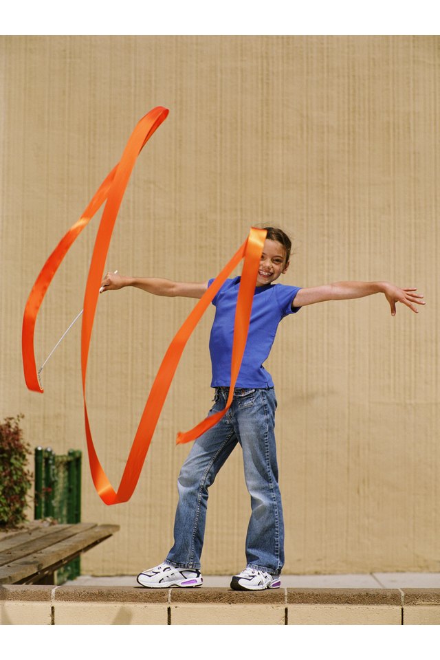 Girl (7-9) standing on wall, pretending to do rhythmic gymnastics