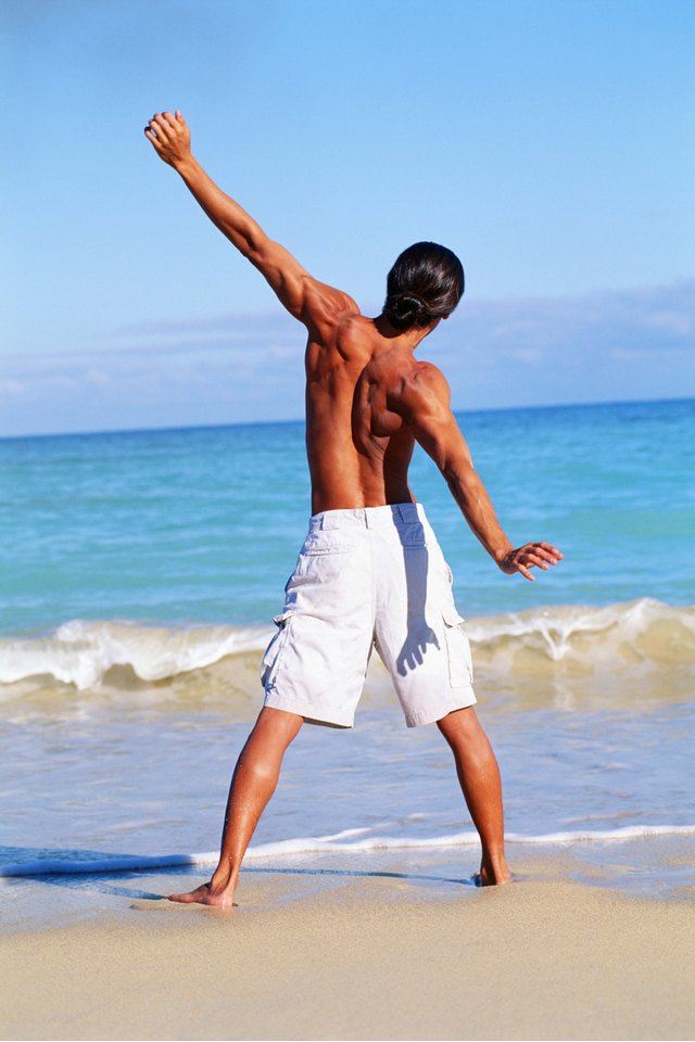 View from back of man wearing only shorts stretching on beach