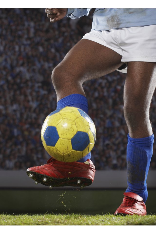 Soccer player kicking ball on field, low section