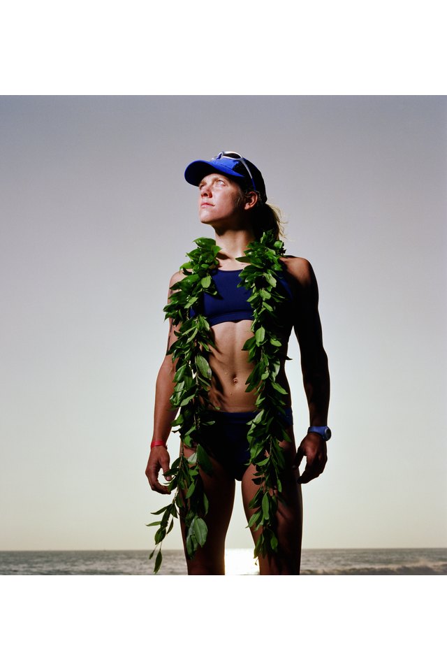 Triathlete wearing ti leaf lei, standing on beach, looking outward
