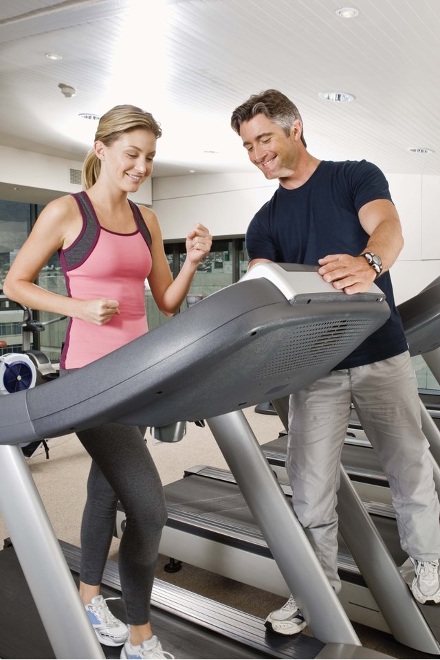 Man assisting woman on treadmill at gym