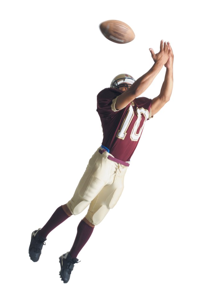 an african american football player in a red and white uniform is jumping up with arms outstretched to catch a football