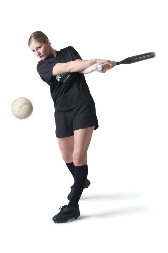 a pretty young caucasian woman is wearing a black softball uniform and swinging her bat after hitting a ball