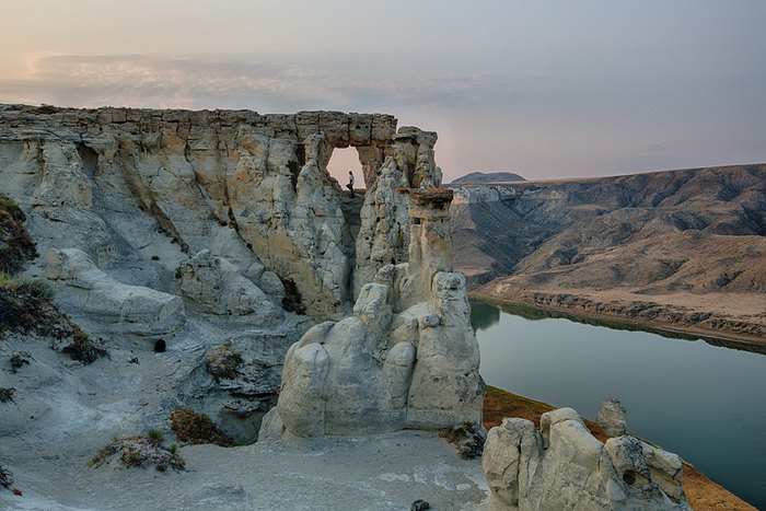 White and multicolored rock pillars line the rim of the Missouri River Breaks National Monument.  A person is standing on top of one of the white cliffs.