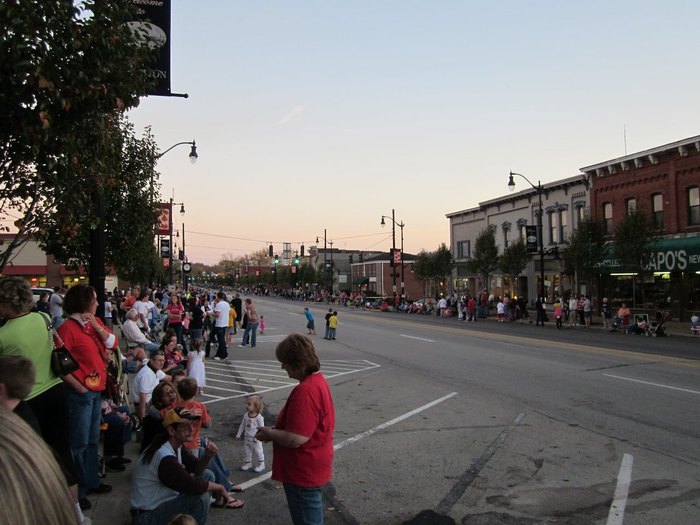 People line an empty street, waiting for a parade.