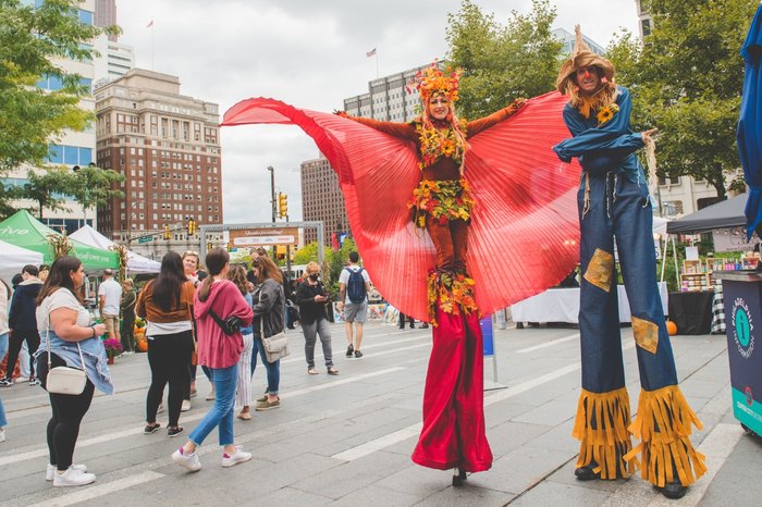 Two festive performers on stilts among a crowded festival.