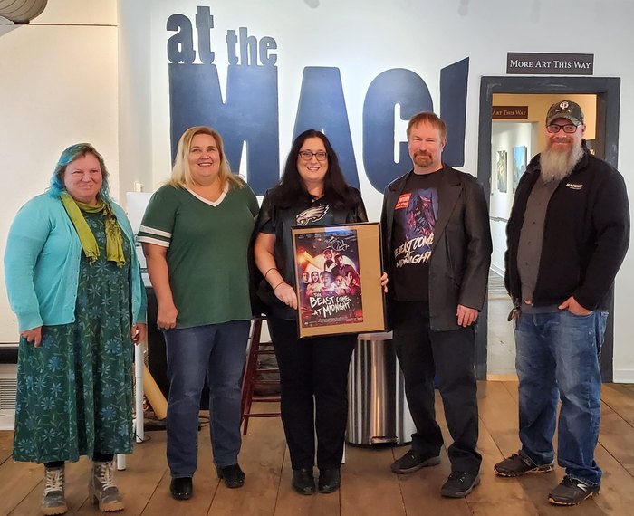A group of smiling people hold a movie poster.