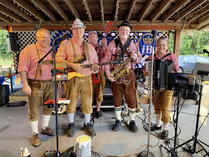 A cheerful band dressed in lederhosen stand on a stage.