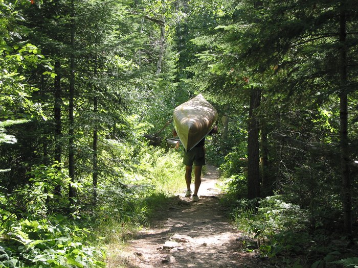 Portaging a canoe through woods in Boundary Waters Canoe Area, Minnesota.
