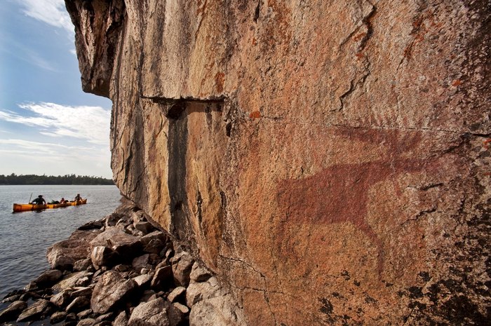 Canoeists paddle by pictographs on Lac La Croix Lake. The pictographs date back several hundred years, and are painted on cliffs on Minnesota's Lac La Croix Lake in the Boundary Waters Canoe Area Wilderness.