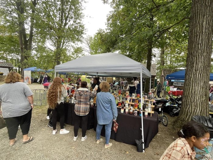 A group of people stand at a tented table, viewing crafts.