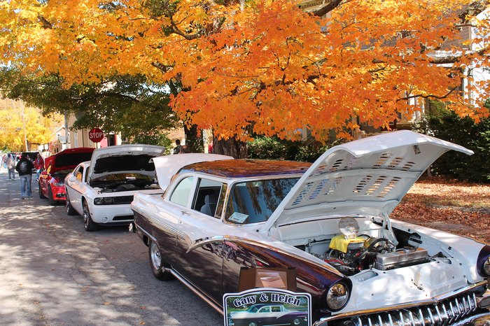 Bright orange leaves hang over a street lined with classic cars.