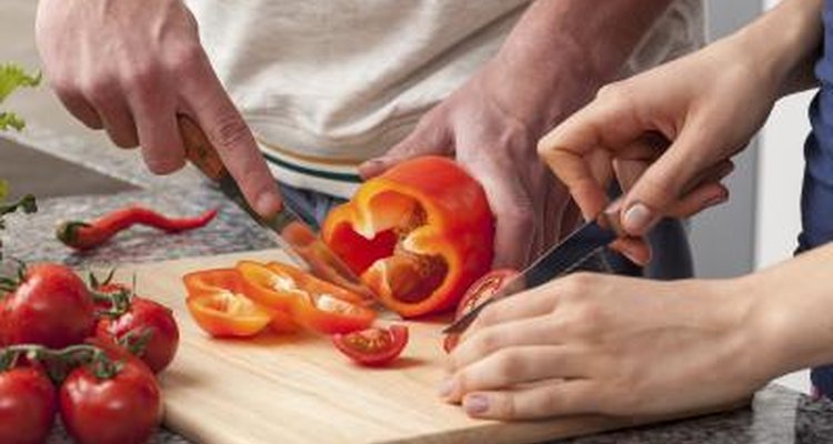 A man and woman sharing a cutting board to chop vegetables together.