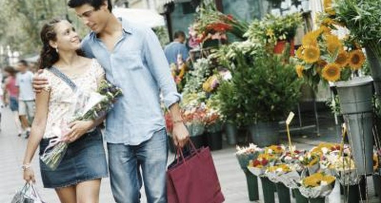 A young couple walks together with shopping bags and flowers.