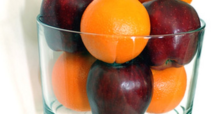 Un bol de vidrio lleno con manzanas y naranjas.