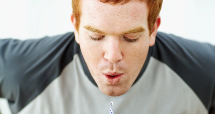 Close-up of a young man blowing candles out on birthday cake