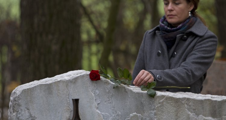 Mature woman placing red rose on gravestone in cemetery