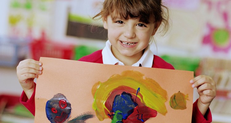 Schoolgirl (4-6) holding painting, smiling, portrait