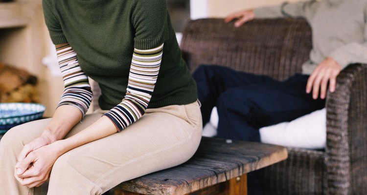 Young woman sitting on a table with a young man sitting on a couch behind her