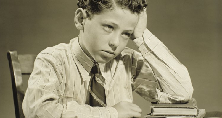 Boy (10-11) sitting at table over open book, head resting on hand, (B&W), close-up