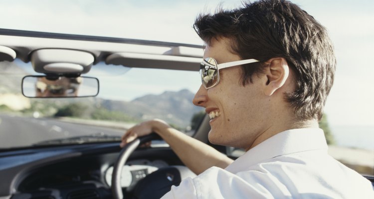 Young man driving in cabriolet car, smiling, rear view