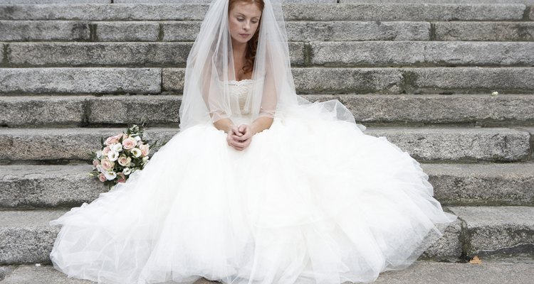 Bride sitting on stone steps, looking towards ground