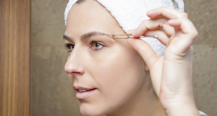 Portrait of girl plucking eyebrows with tweezers