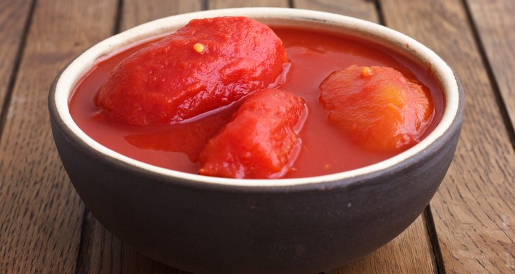 Whole canned tomatoes in brown bowl on wood.