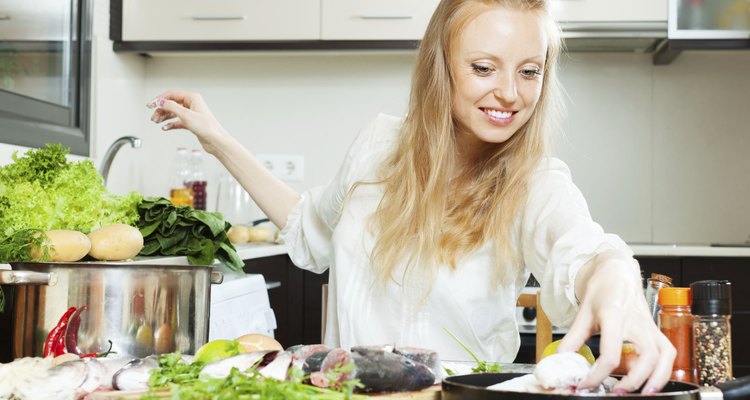 Happy woman putting  fish in flour into frying pan