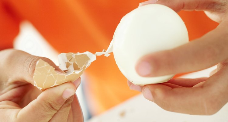 Close-up of a person's hands peeling the shell of a boiled egg