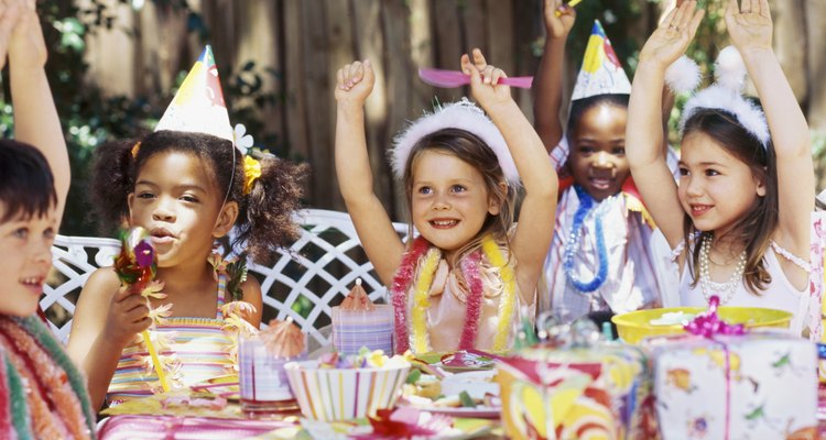 Group of children sitting at a table at a birthday party with their arms raised
