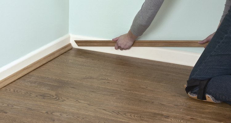 Finish laminate flooring around the edge of the room with trim.