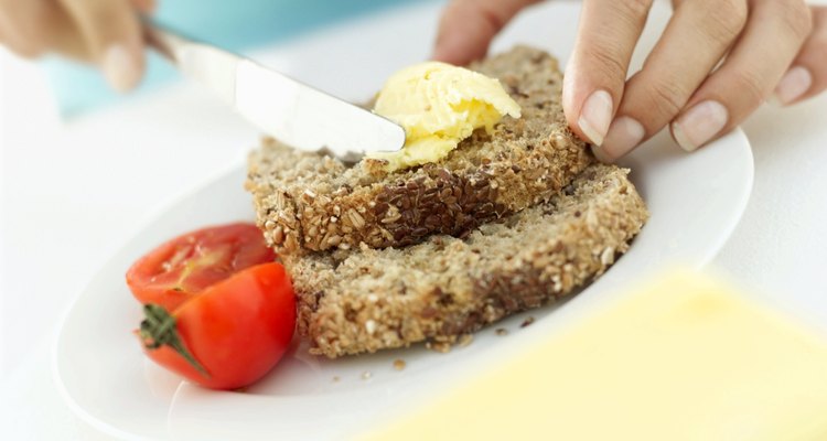 Close-up of a human hand spreading butter on sliced whole wheat bread