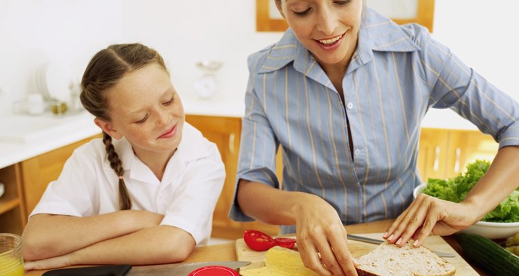 Young mother making a ham sandwich with a young girl (8-10) watching her