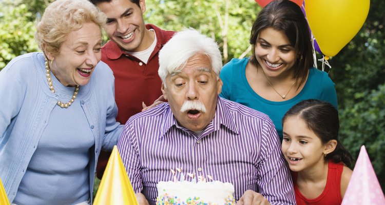 Senior Hispanic man blowing out birthday candles with family in park