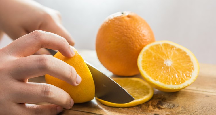Hand slicing orange on wooden board