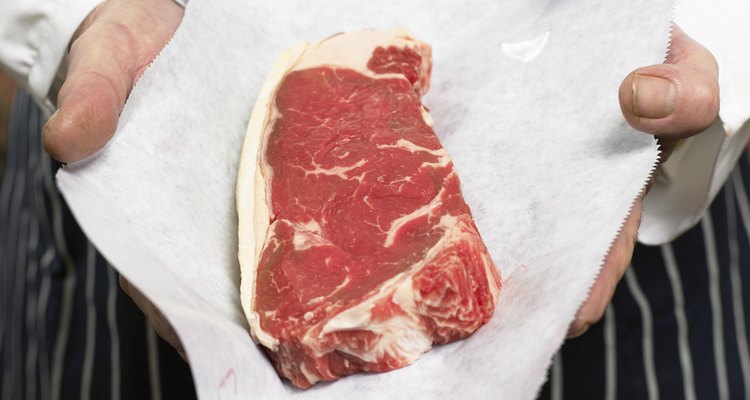 Senior male butcher holding sirloin of steak, mid section