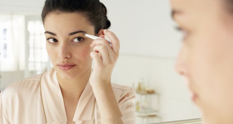 Young woman plucking eyebrows, close-up, reflection in mirror